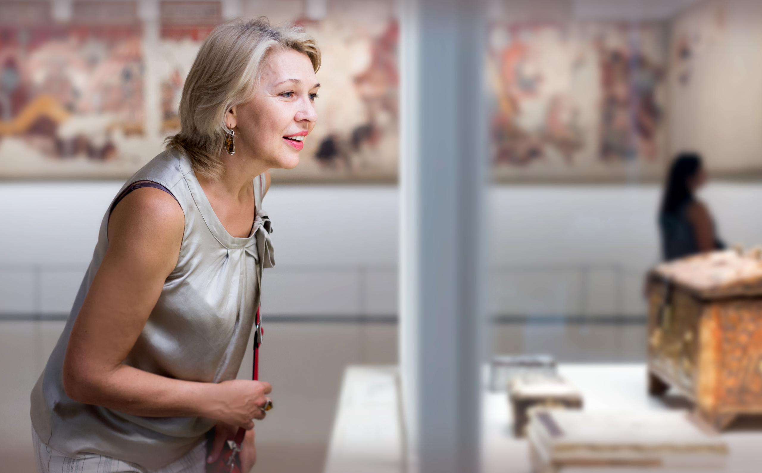 Woman admiring a museum-quality artifact in a softly lit gallery — capturing the sense of discovery and wonder that antiques fairs evoke.