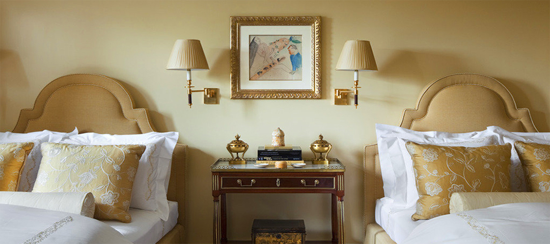 Symmetrical bedroom vignette featuring antique bedside tables, classic lamps, and framed art, demonstrating how timeless furnishings create warmth, balance, and sustainability through reuse.