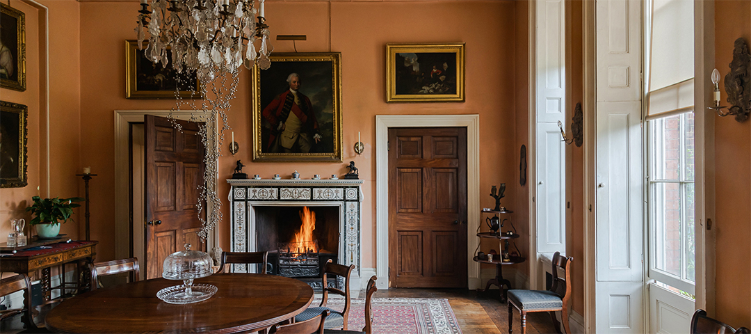 Georgian-style interior with paneled doors, crystal chandelier, portrait paintings, and a lit fireplace at the Bath Decorative Antiques Fair.