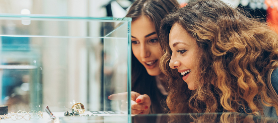 Collectors examining antique jewelry inside a glass case at a US antique show.