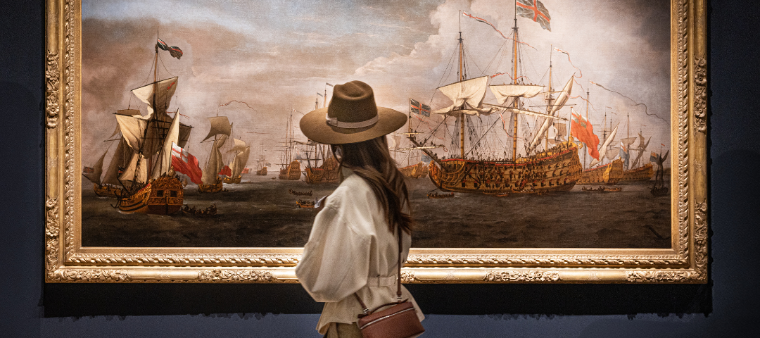 Visitor observing a large framed historic maritime painting at a vetted European art and antiques fair, highlighting scholarship and museum-caliber presentation.