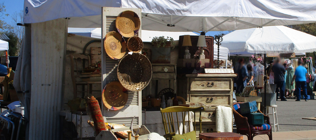 Open-air antiques fair with dealers displaying furniture and decorative objects under tents, representing large-scale trade-focused sourcing in the UK and EU.
