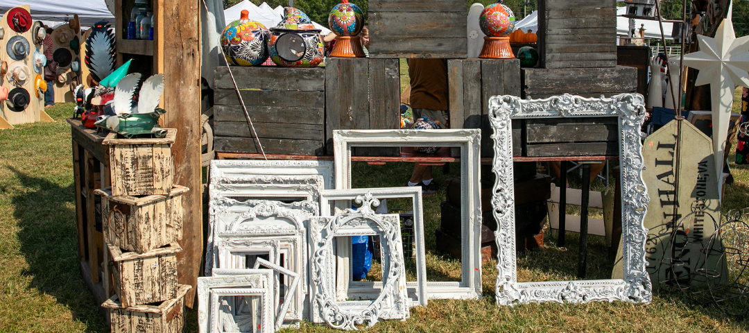 Outdoor flea market stall displaying vintage mirrors, painted wooden frames, and decorative objects arranged against rustic crates.