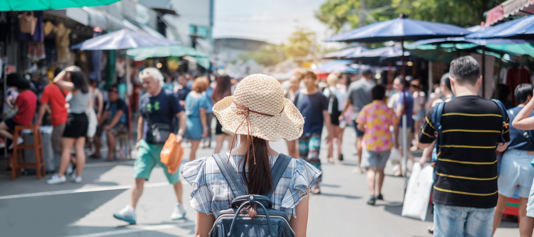 Crowded outdoor flea market with shoppers exploring vendor stalls offering vintage items and antiques.