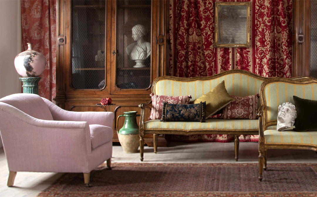 Layered interior featuring antique furniture, including a striped sofa, upholstered armchair, wood cabinet, and classical bust, styled to reflect the character and context of one-of-a-kind pieces.