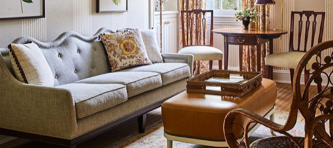 A traditional living room with a tufted sofa, antique side chairs, and a leather ottoman, showcasing a mix of periods and materials that create depth and character.