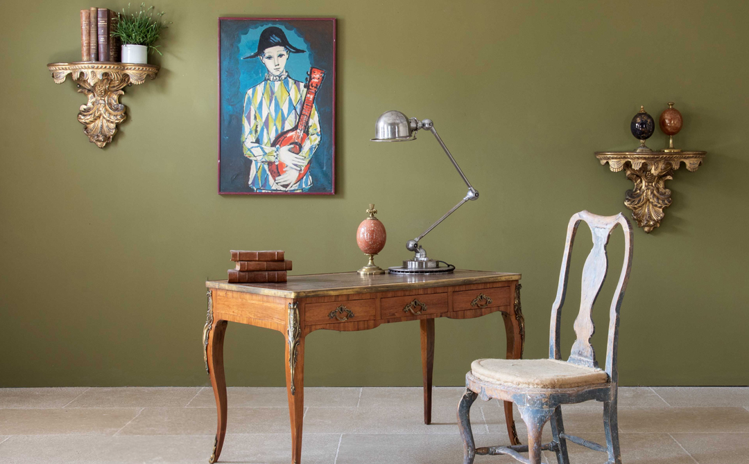 Eclectic interior featuring an antique French writing desk, distressed side chair, gilt wall brackets, and colorful modern artwork — illustrating the layered, collected interiors discussed in Ronati’s exploration of AI, authenticity, and material character in design.