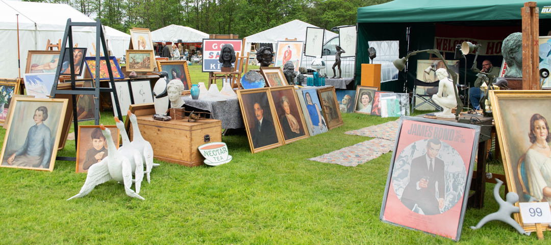 Open-air fair stand featuring a mix of framed artwork, sculpture, and decorative objects arranged for browsing and sourcing
