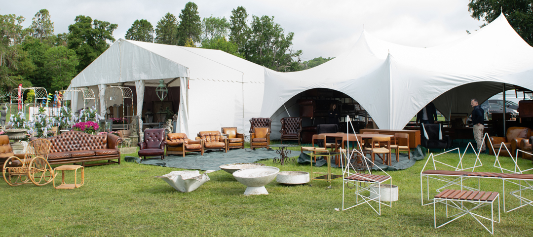 Selection of vintage and antique furniture displayed across outdoor tents, including leather seating, tables, and modern metal pieces
