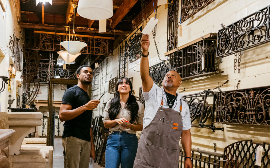 Dealer guiding two clients through a showroom of architectural antiques, demonstrating how expertise and firsthand evaluation help buyers understand the history, craftsmanship, and authenticity of antique objects.