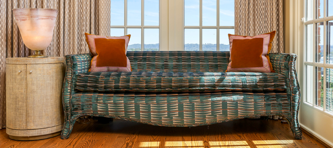 Michelle Workman sitting room with sofa in patterned teal velvet with nailhead trim and serpentine legs, beside a cylindrical parchment lamp, framed by a window with hill views.