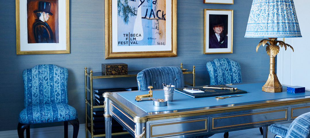Study created by Alex Papachristidis with blue grasscloth walls, a steel-and-brass desk, a gilt palm lamp, and a gallery wall of framed art.