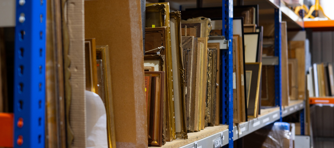 Stored antique frames and artwork in warehouse shelving, illustrating hidden inventory waiting to be documented, organized, and made visible to buyers.