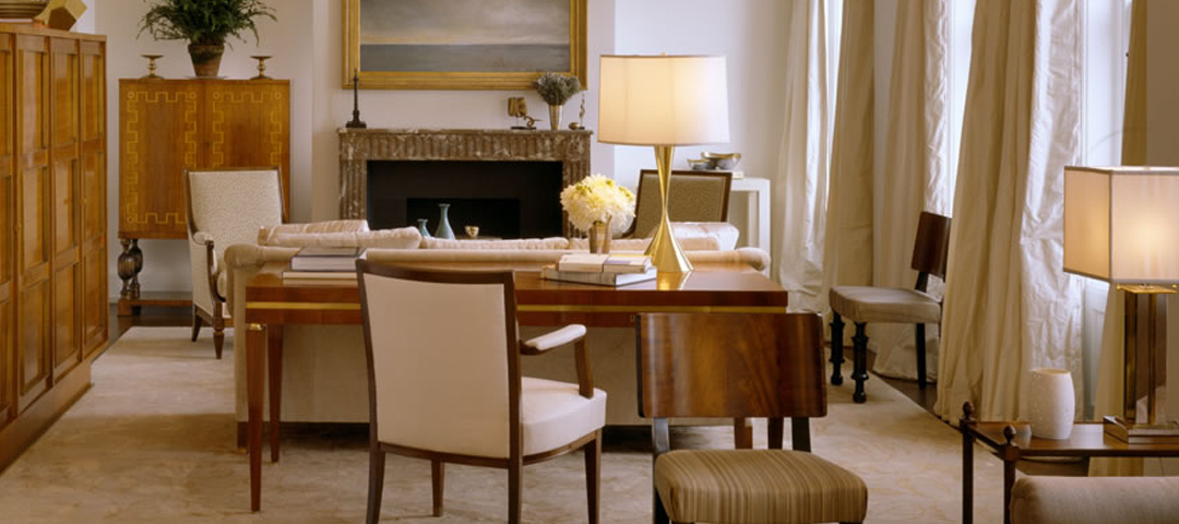 Room designed by Alex Papachristidis anchored by figured-wood Art Deco furniture — a Greek-key cabinet and flip-top desk — beside a marble fireplace.