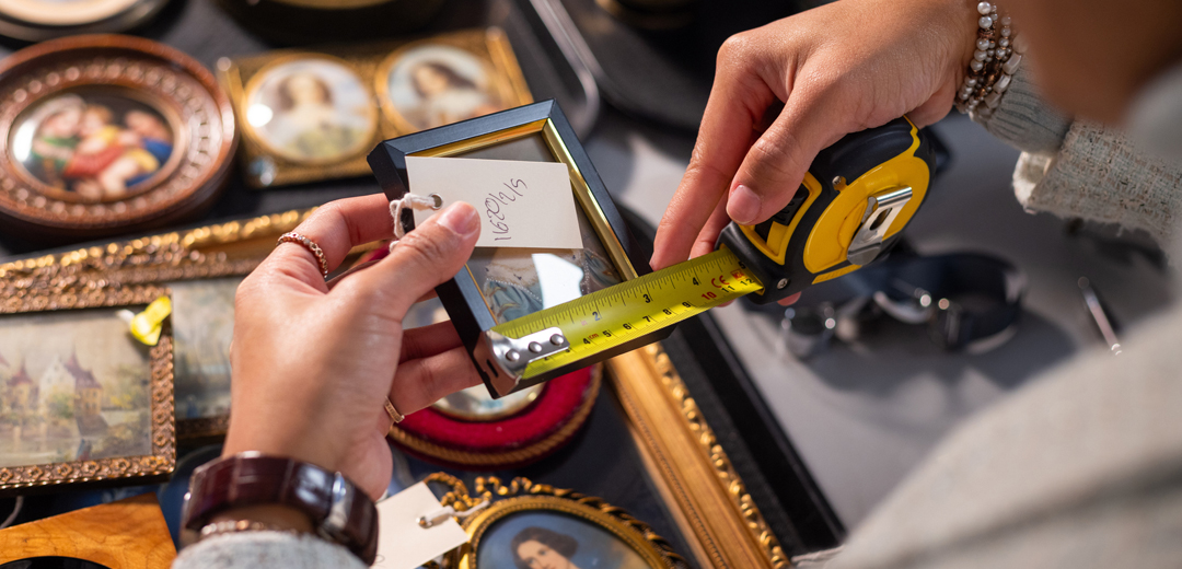 Collector measuring a framed antique object while reviewing inventory, reflecting the documentation, research, and attention to detail that support accurate attribution and provenance records.