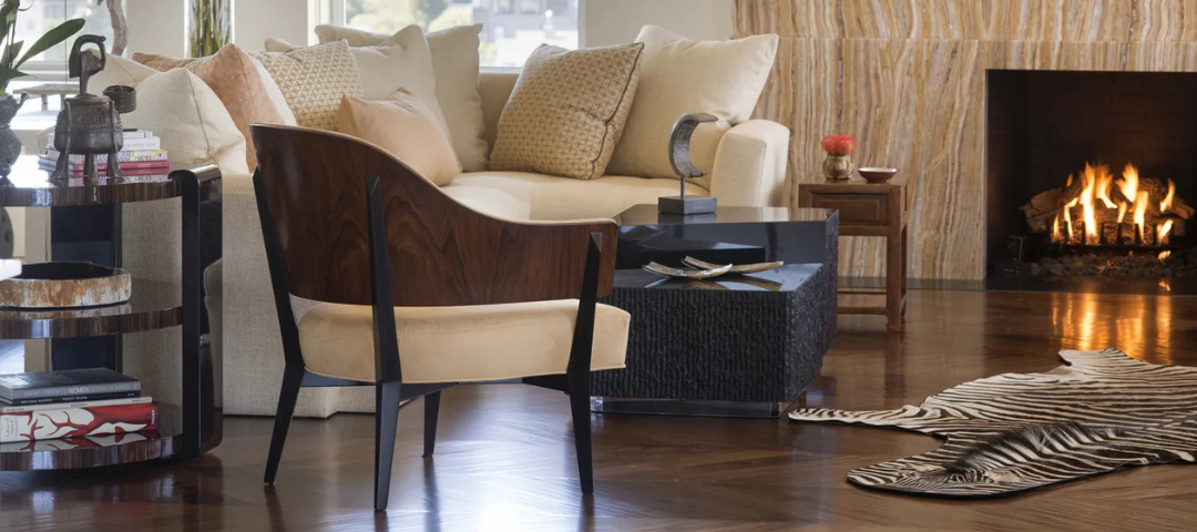 Living room with a curved rosewood armchair, cream sofa, black textured cocktail table, and a zebra hide rug over dark wood floors. Created by Tucker and Marks.