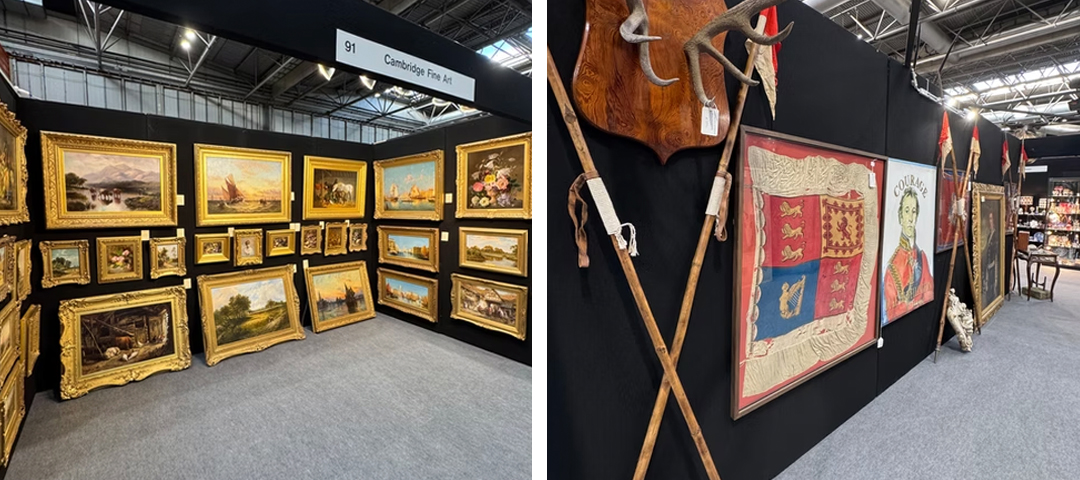 Gilt-framed landscape and still life paintings at a Cambridge Fine Art booth, alongside framed regimental flags and antlers at an antiques fair