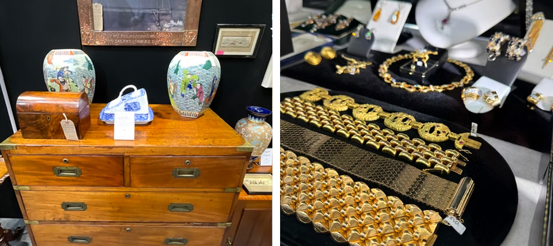 Antique Chinese porcelain vases and a tea caddy on a wooden chest, alongside a display case of gold statement jewelry at an antiques fair