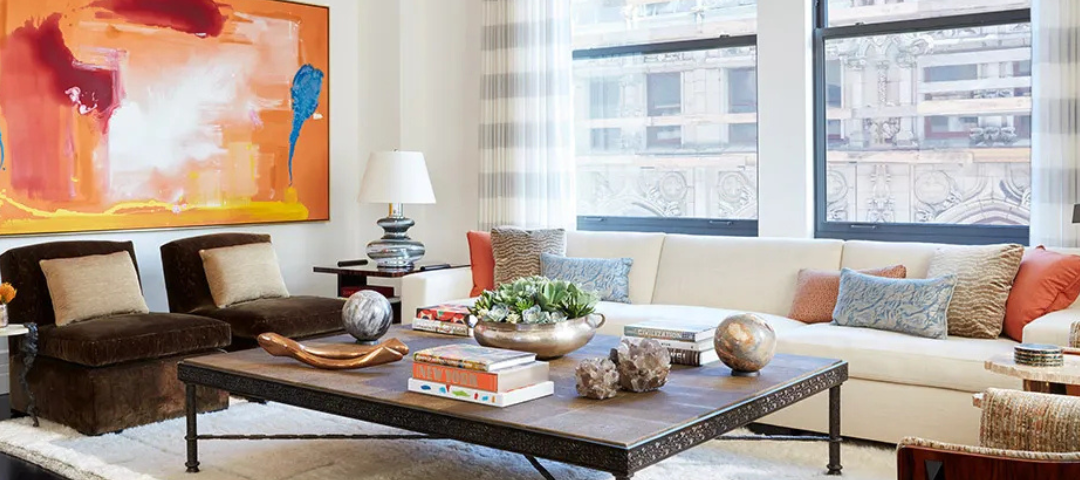Living room with a large abstract painting, brown velvet slipper chairs, and a low table layered with books, quartz specimens, and bronze objects. Created by Tucker and Marks. 
