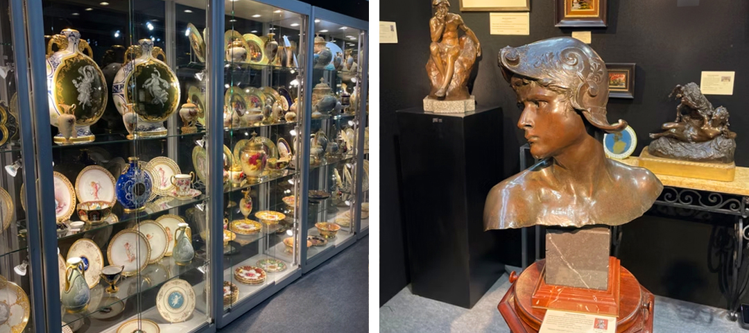 Glass display cabinet of hand-painted porcelain plates and vases, next to a bronze bust sculpture wearing a helmet at an antiques fair