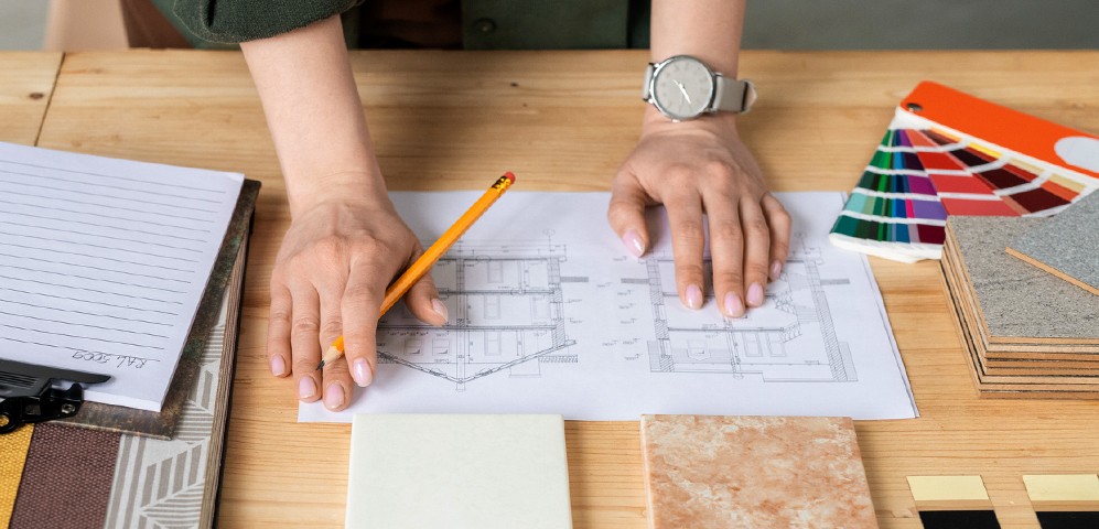 Designer sketching on floor plans surrounded by fabric swatches and material samples.