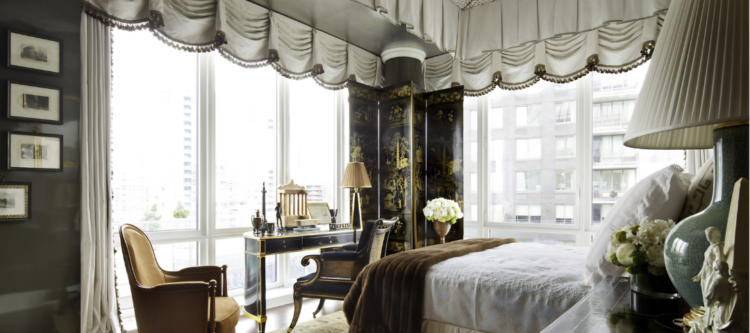Alexa Hampton's Kips Bay bedroom, where a Louis XVI leather tub chair on fluted legs and a caned armchair sit against floor-to-ceiling windows and a Manhattan skyline.