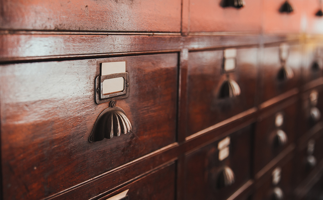 Close-up of an antique wooden card catalog drawer with a brass label holder and pull, showing hand-finished joinery and decades of patina.