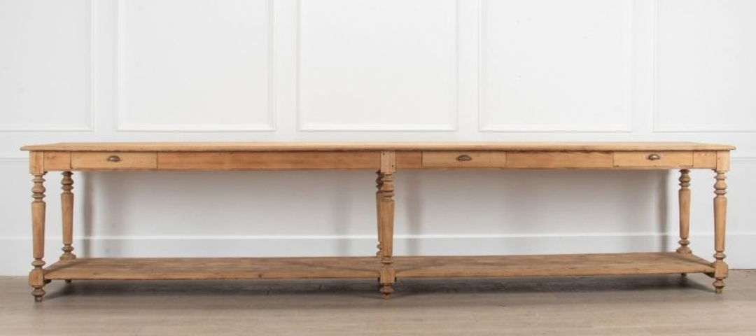 An extra large 19th-century pitch pine drapers' table from Lorfords, with turned legs, three drawers, and a lower shelf, against a white paneled wall
