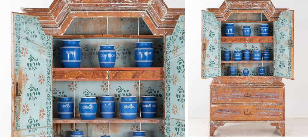 Open painted Swedish cupboard with floral stenciling, shelves lined with antique blue-and-white storage jars.