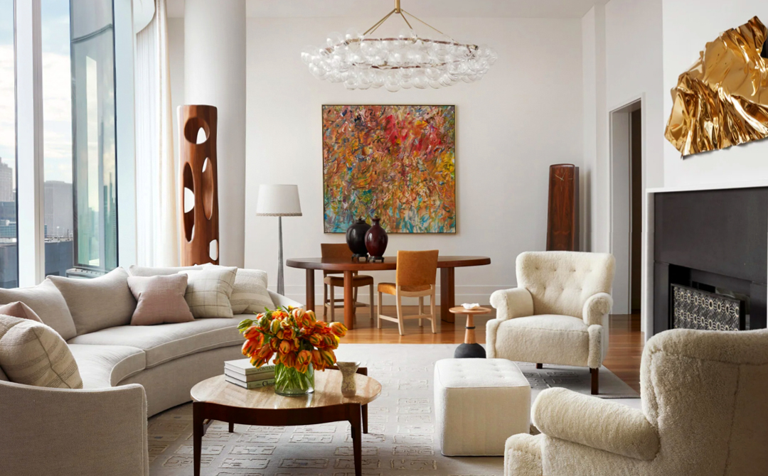 Living room by [Designer] pairing carved wood sculptures and an abstract painting with shearling armchairs, a curved sofa, and city views.