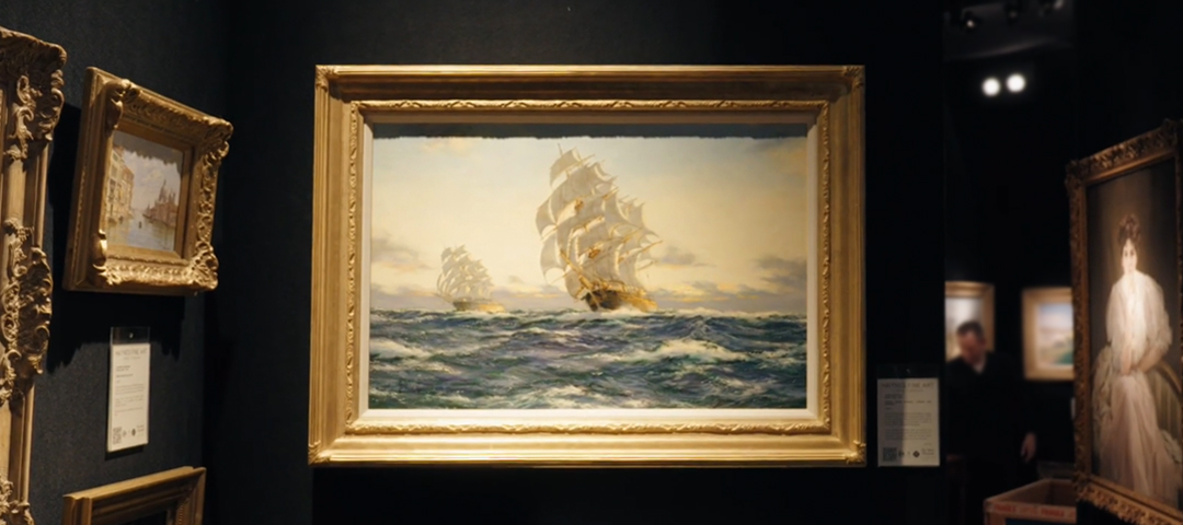 Gilt-framed marine painting of two tall ships under full sail on rough seas, displayed in a dealer’s booth beside smaller framed works